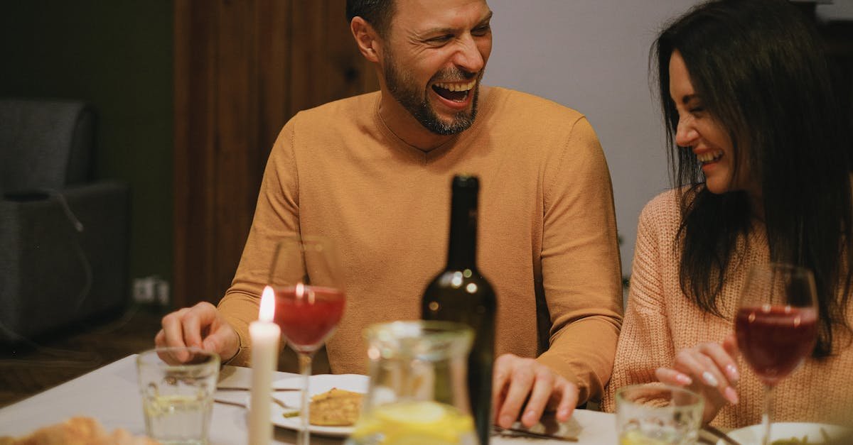 A joyful couple shares laughter and affection during a cozy dinner with wine and candlelight.