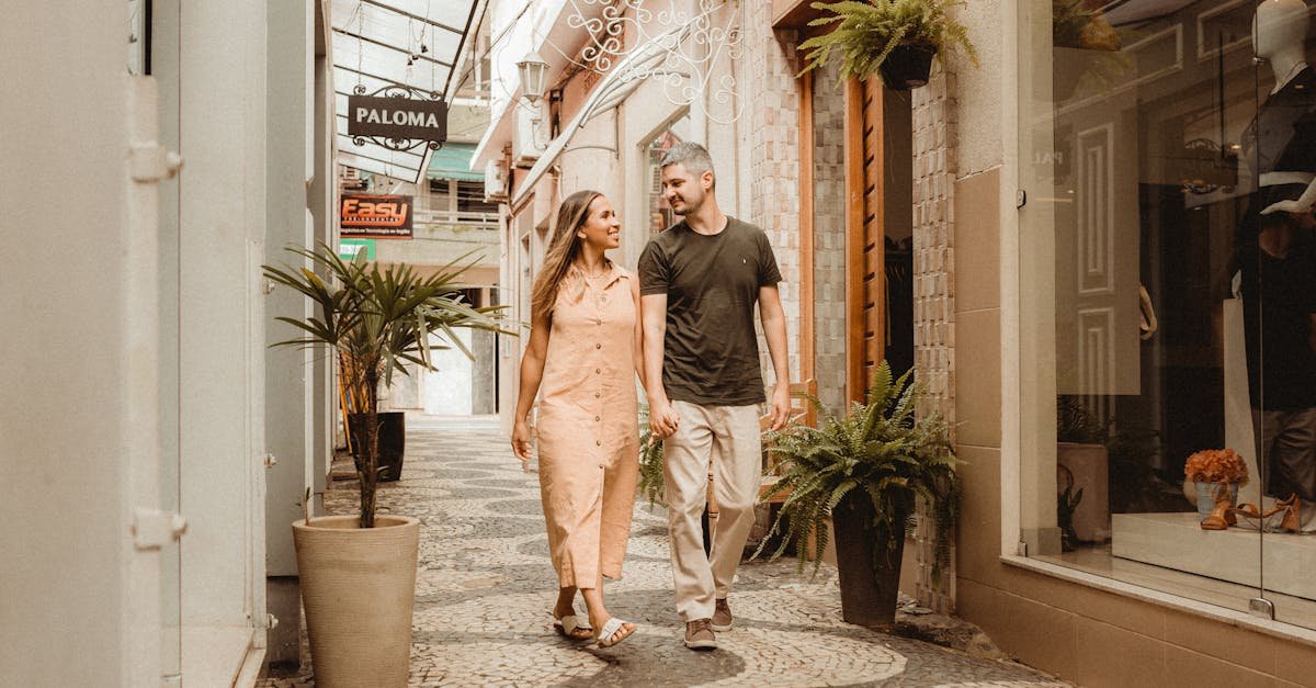 A joyful couple walks hand-in-hand through a charming city alley lined with shops and greenery.