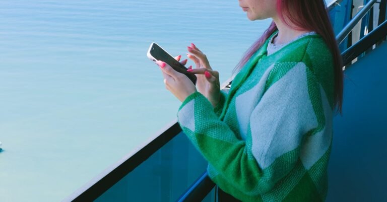 Woman using a smartphone on a balcony with a tranquil ocean view.