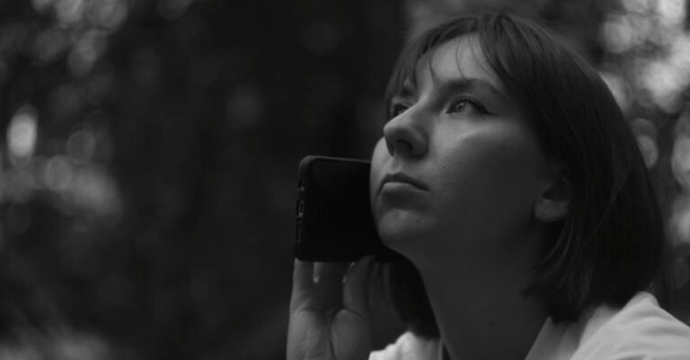 Grayscale portrait of a woman holding a smartphone, looking thoughtful outdoors.