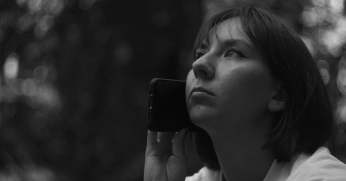 Grayscale portrait of a woman holding a smartphone, looking thoughtful outdoors.