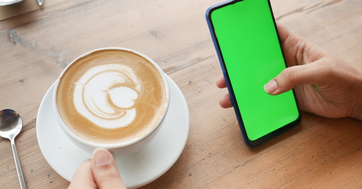 Close-up of a latte and a smartphone with a green screen on a wooden table.