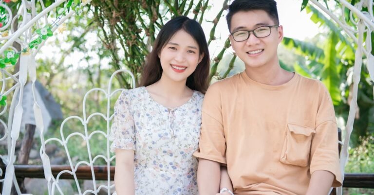 Smiling Asian couple sitting on a swing, holding hands in a lush garden.