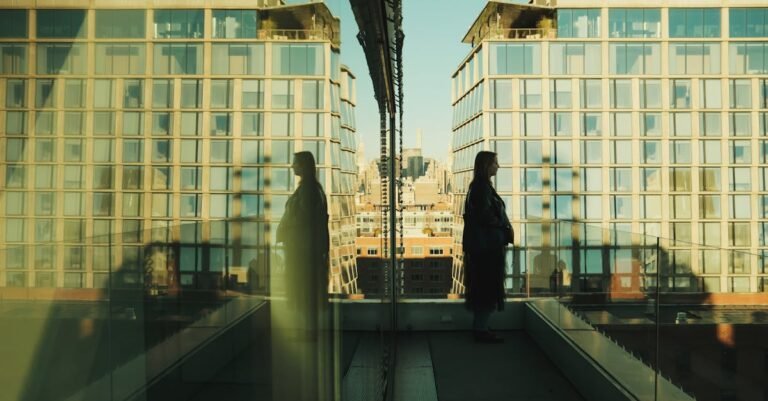 A woman stands on a New York balcony with reflections on a glass facade, showcasing an urban skyline.
