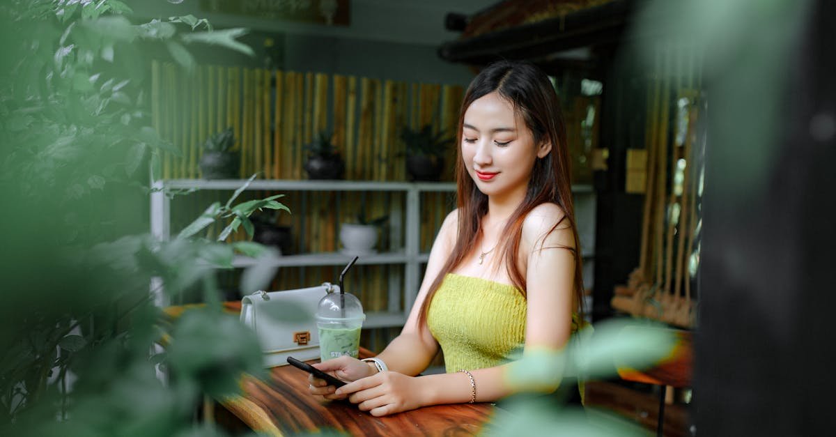 Young woman using smartphone in a vibrant café with plants and refreshing drink.