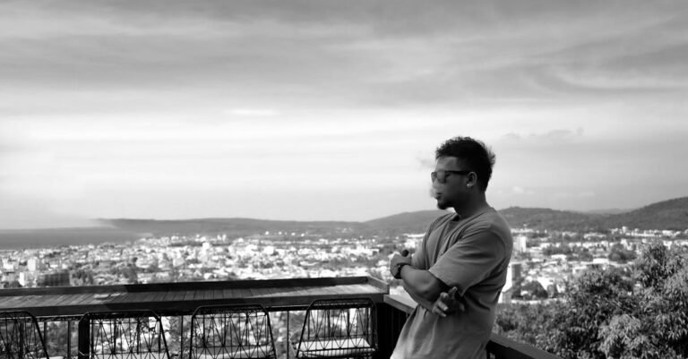 Man standing on a balcony overlooking a city in black and white.