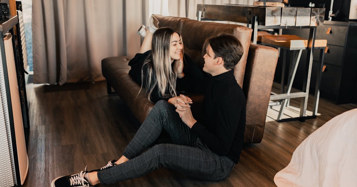 A couple sits lovingly on the floor by a sofa in a cozy room, capturing moments of togetherness.