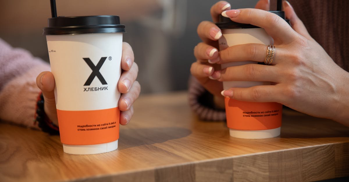 Two people hold takeaway coffee cups with drink straws in a cozy setting.