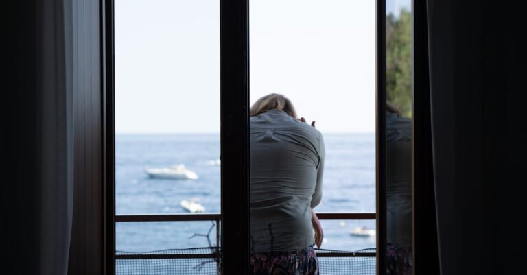 A woman sits thoughtfully on a balcony overlooking the serene Campania sea, Italy.