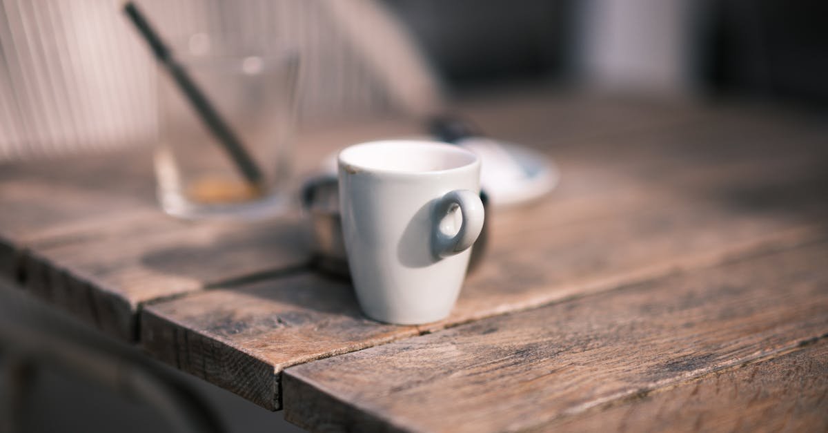 Close-up of a white coffee cup on a wooden cafe table, capturing a cozy outdoor ambiance.