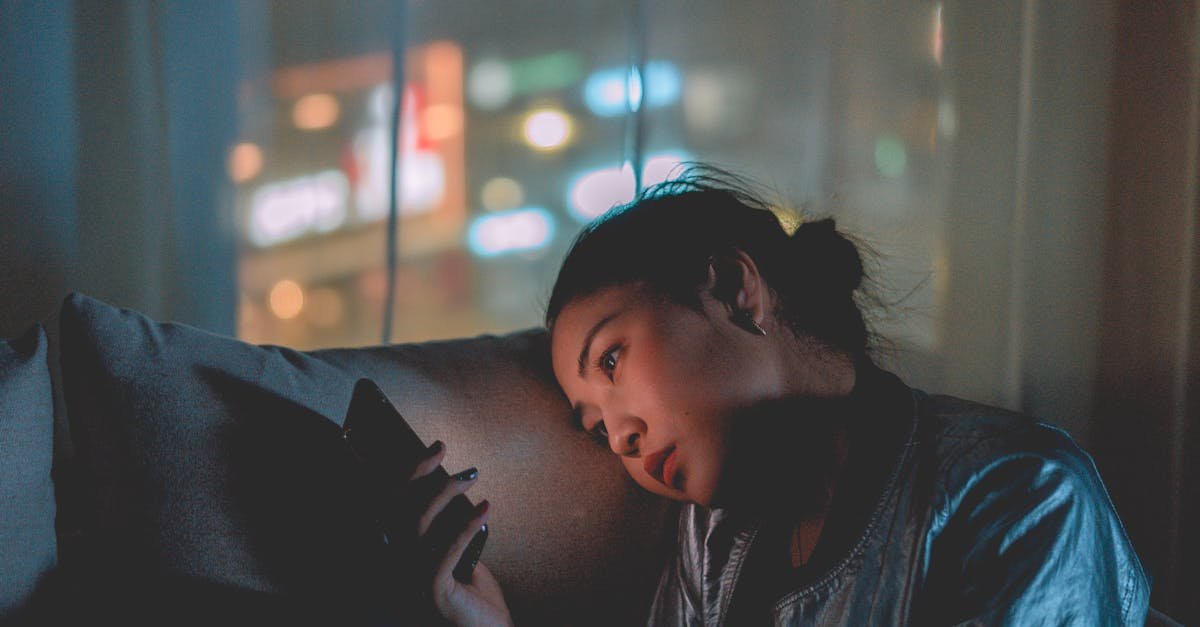 A woman looking at her mobile phone at night with city lights blurred in the background.