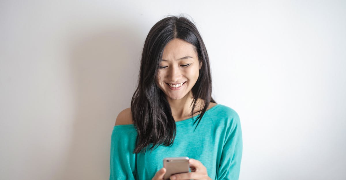 A happy woman in a green top smiling while using her smartphone indoors.