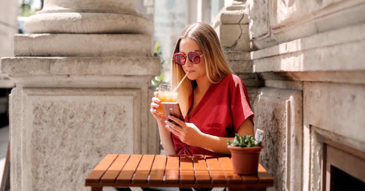 Woman sipping a drink while browsing on her smartphone at an outdoor cafe table.