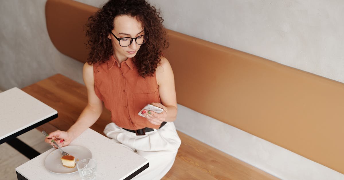 Woman with curly hair enjoys dessert while checking smartphone in a stylish cafe.