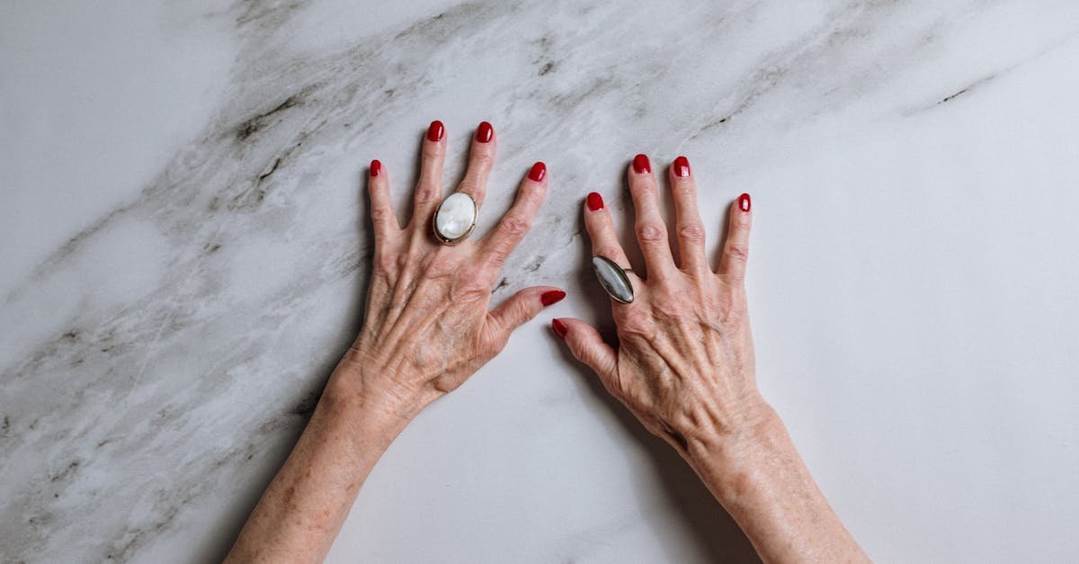 Elderly woman's hands with red nails and rings set against a marble background.