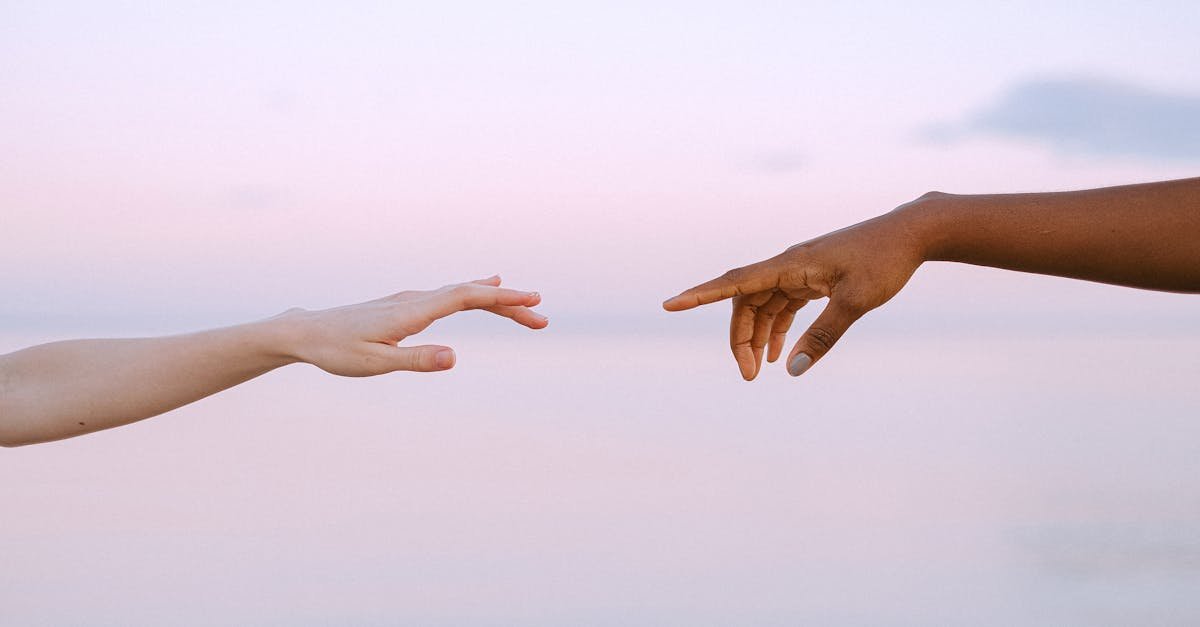Two diverse hands reaching out across a pastel horizon, symbolizing unity and connection.