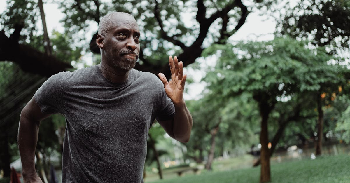 Senior man running through a lush green park, focused on fitness and wellbeing outdoors.