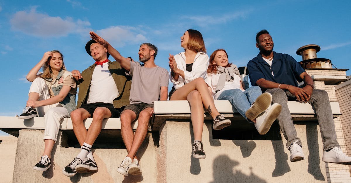 A diverse group of friends laughing and enjoying a sunny day on a rooftop with a blue sky background.