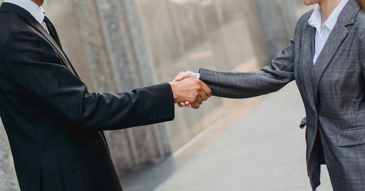 Man and woman in business attire shaking hands outdoors.