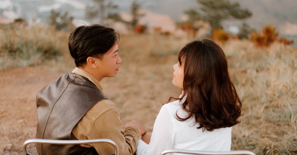 Back view of loving ethnic couple sitting together on chairs and enjoying each other while looking at each other