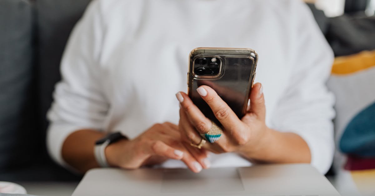 Close-up of a woman holding a smartphone and using a laptop indoors.