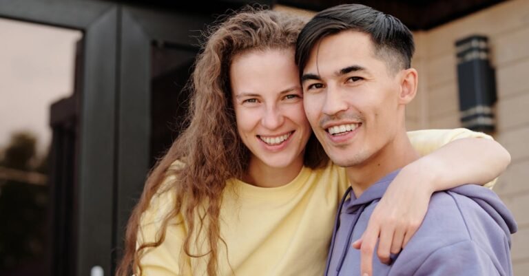 Smiling couple in casual attire embracing outdoors, showcasing love and happiness.