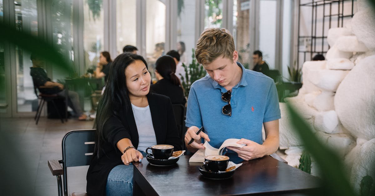 A young couple sits at a café table, sipping coffee and reading together.