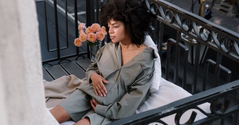 Serene portrait of a pregnant woman sitting on a cozy balcony in the city with flowers nearby.