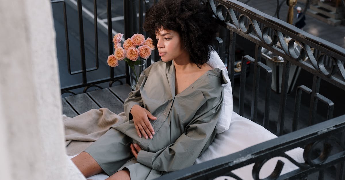 Serene portrait of a pregnant woman sitting on a cozy balcony in the city with flowers nearby.