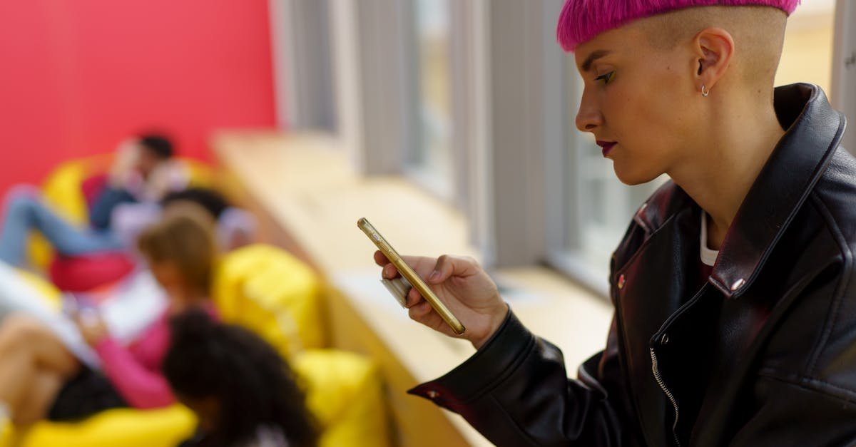 A stylish woman with pink hair uses her smartphone while sitting indoors on bright bean bags.