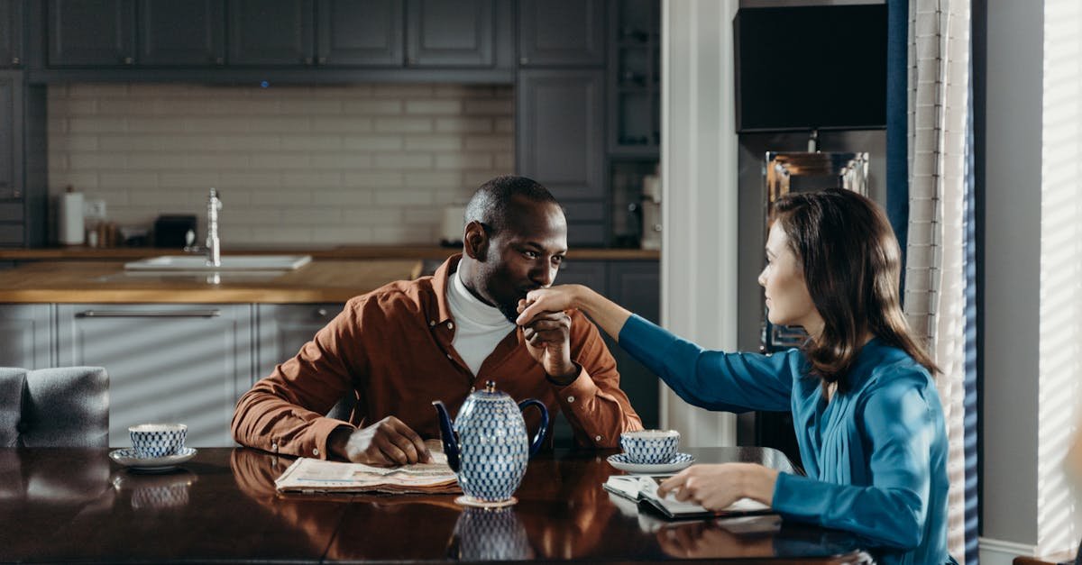 A romantic couple sharing a moment over tea at a wooden table in a cozy kitchen.