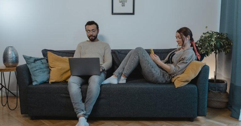 A couple relaxing on a sofa using laptop and smartphone at home. Cozy indoor setting.