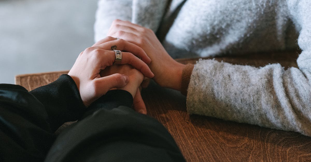 Close-up of two people holding hands on a wooden table, symbolizing connection and warmth.
