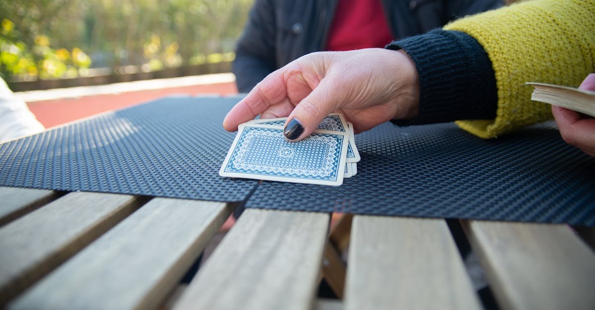 A close-up view of hands playing with playing cards outdoors on a sunny day.