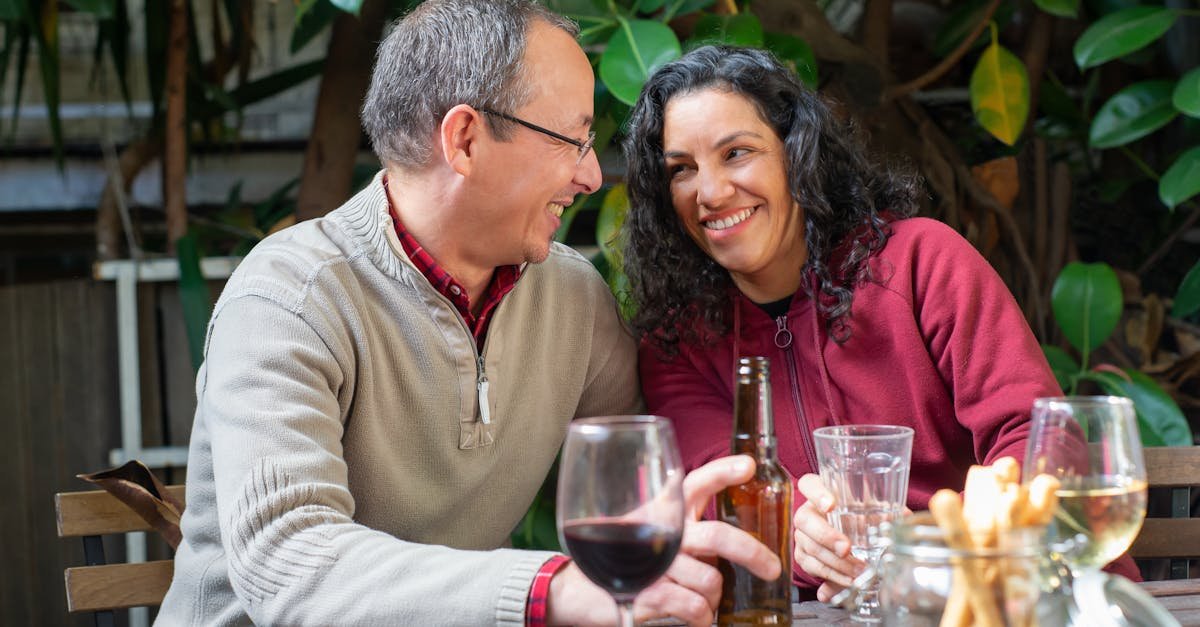 A cheerful couple sitting at a table, sharing smiles over wine and beer in an outdoor backyard.
