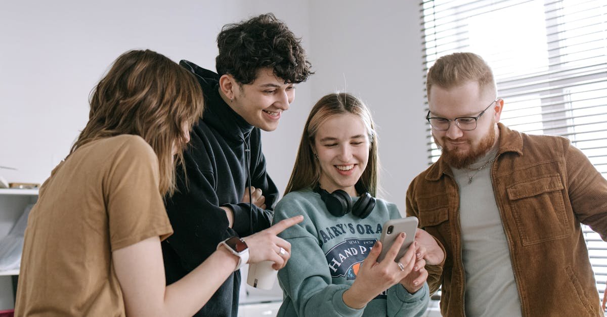 A group of young adults engaged in a cheerful interaction at the workplace, sharing moments on a smartphone.