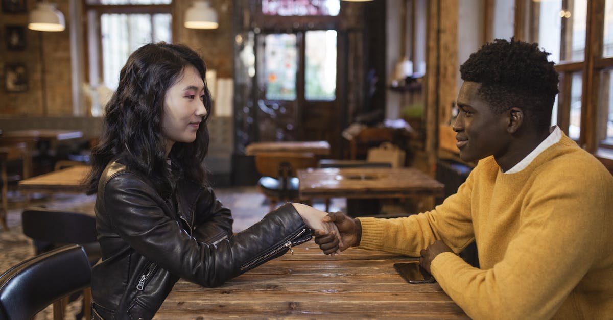 A diverse man and woman sit in a café, shaking hands and smiling warmly.