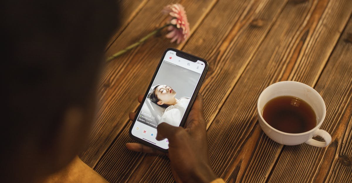 An individual using a dating app on a smartphone with a cup of tea nearby on a wooden table.
