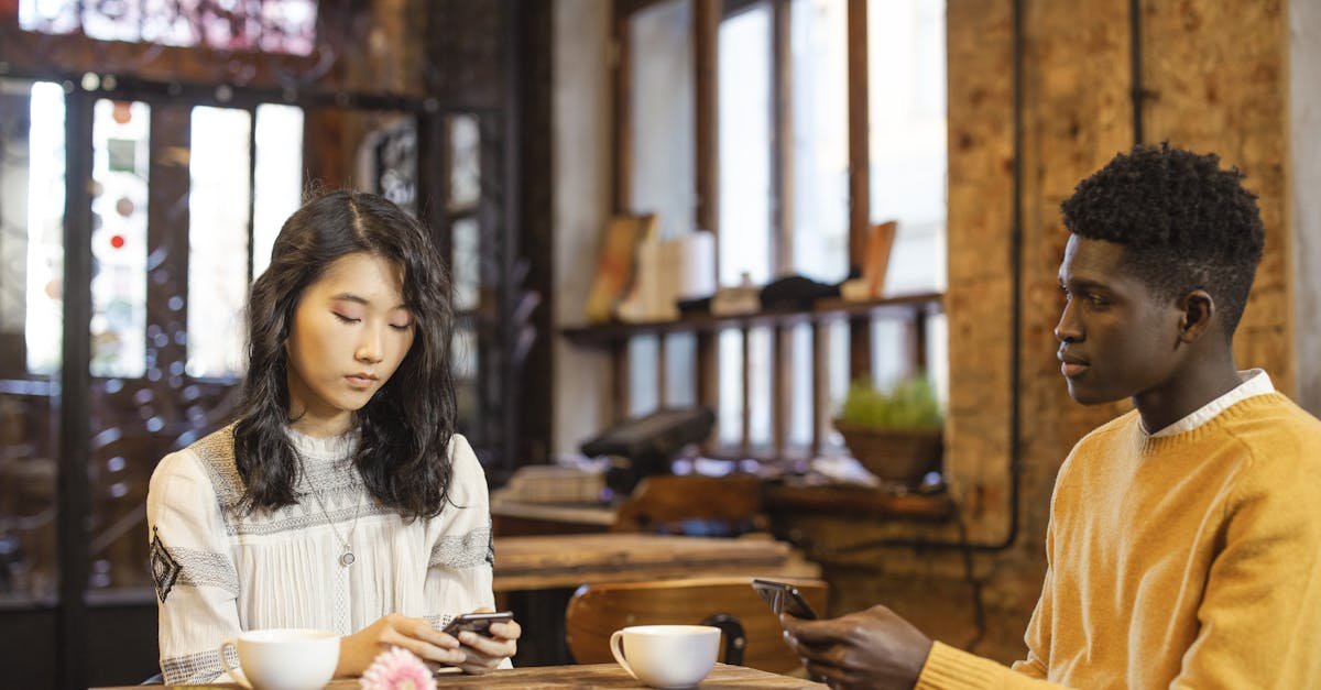 Young interracial couple in a cafe, using phones on a date. Warm setting with a rustic interior.