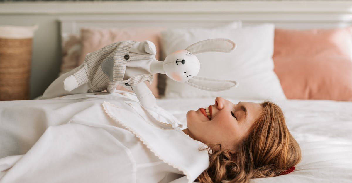 A smiling woman lying in bed holds a playful hand puppet, creating a cozy atmosphere.