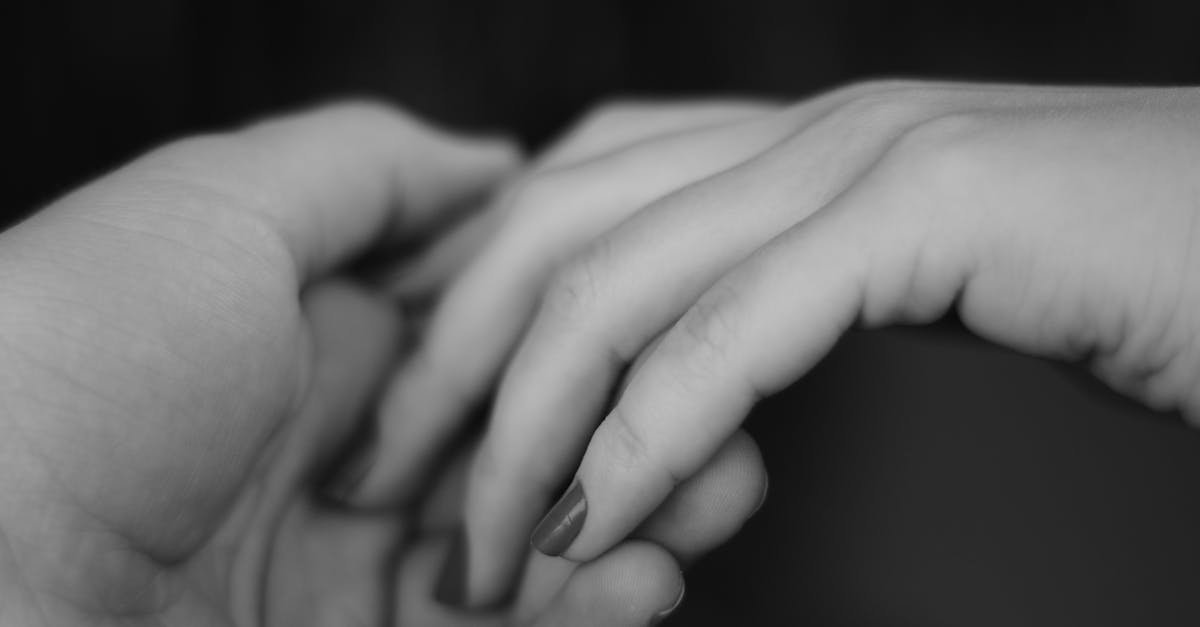 A close-up grayscale photograph capturing the gentle touch and connection of two hands holding each other.
