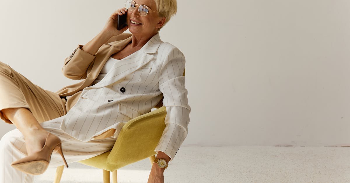 Elegant businesswoman in stylish outfit sits comfortably, smiling and talking on her phone indoors.