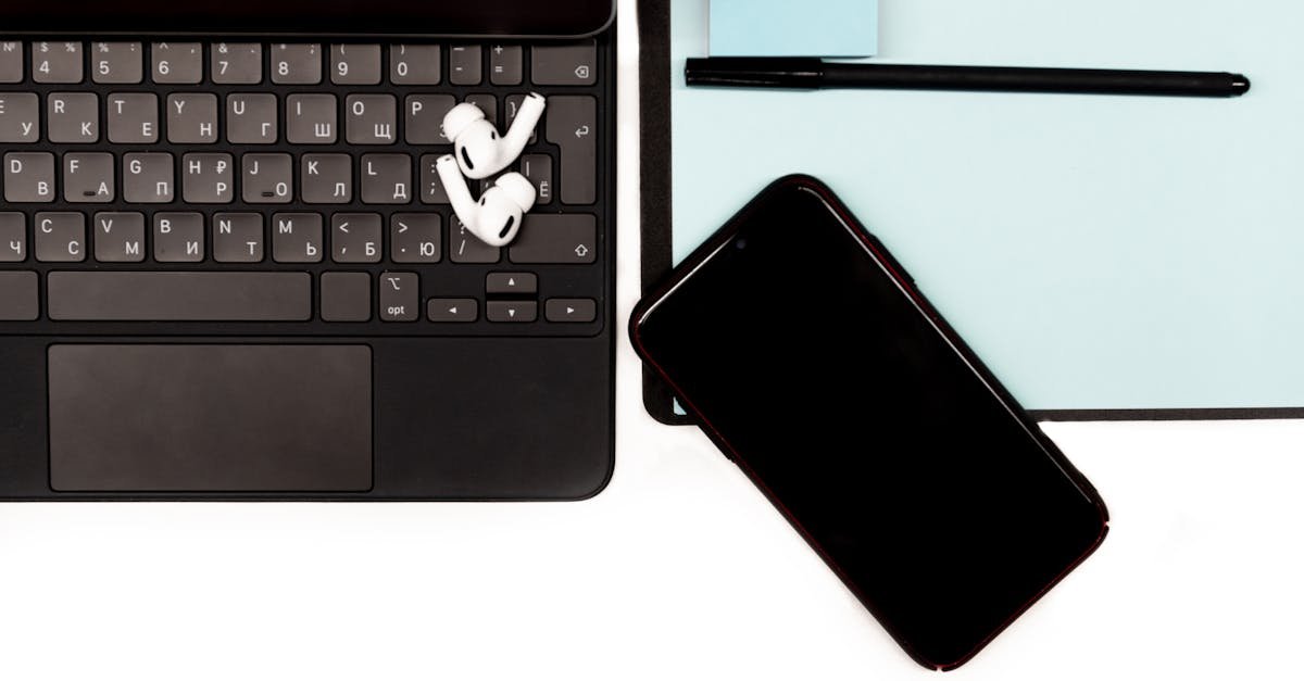 Close-up of a workspace featuring a laptop, smartphone, and wireless earbuds on a desk.