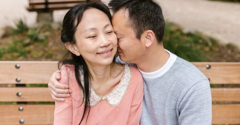 A joyful Asian couple sharing a tender moment on a park bench outdoors.