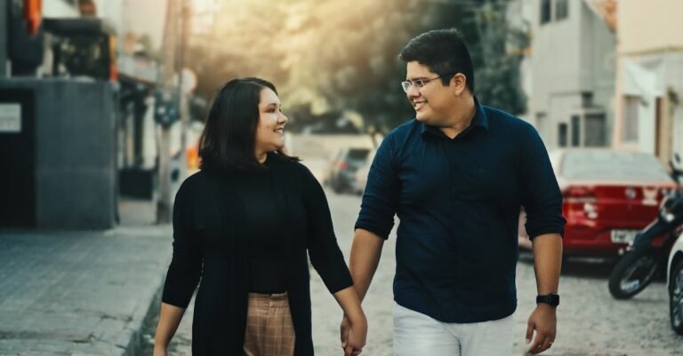 A happy couple holding hands and smiling at each other while walking down an urban street.