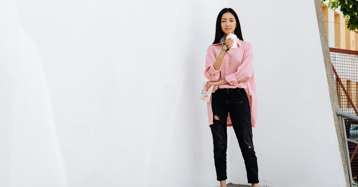 Stylish Asian woman in casual wear posing outdoors while enjoying a coffee.