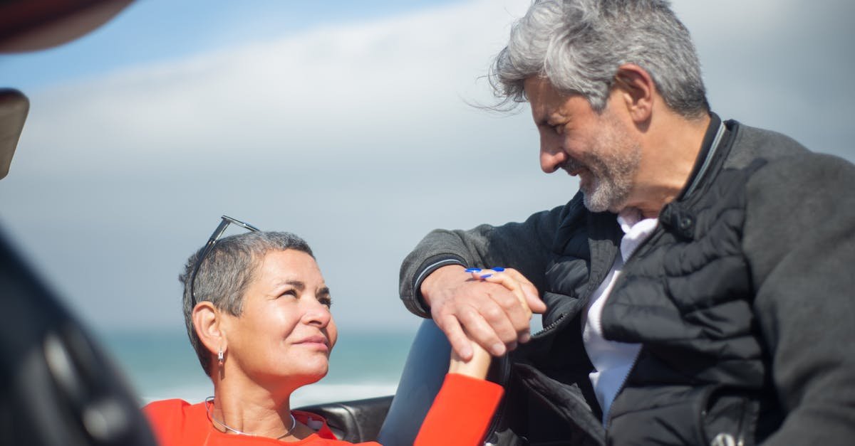Smiling couple holding hands and looking at each other by the ocean, showcasing love and connection.