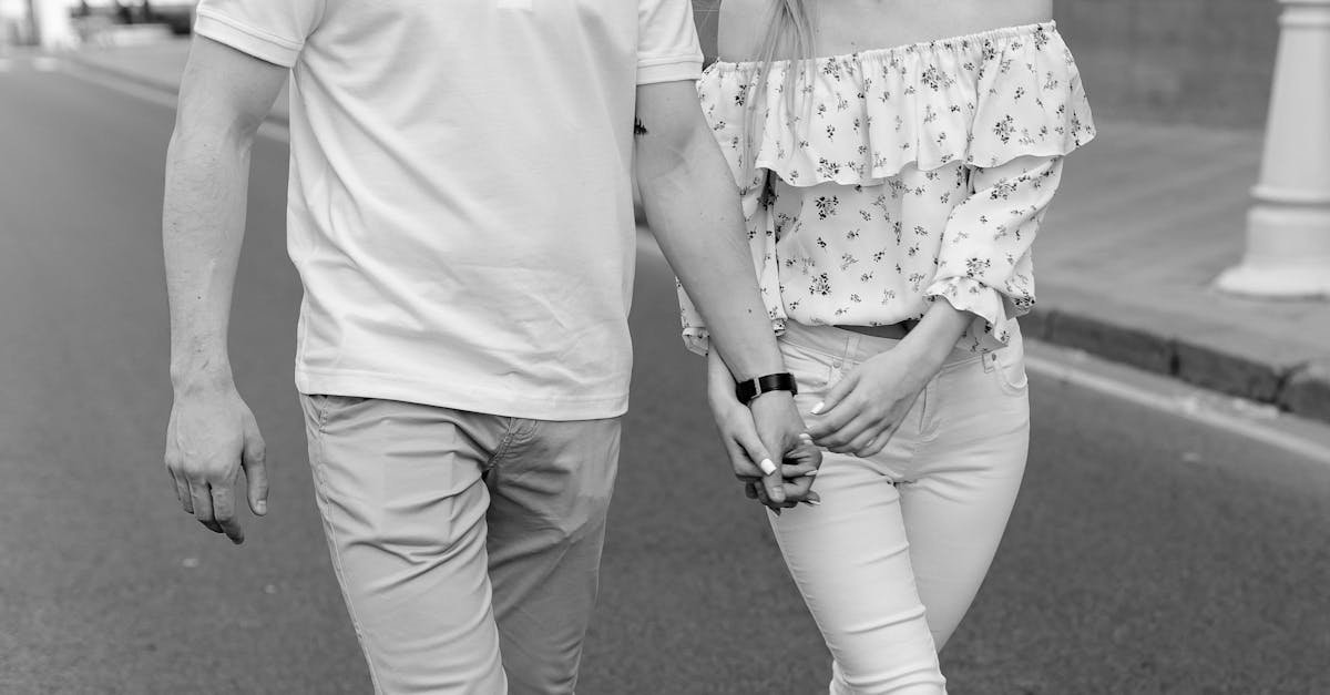 Black and white image of a young couple holding hands while walking outdoors in a city setting.