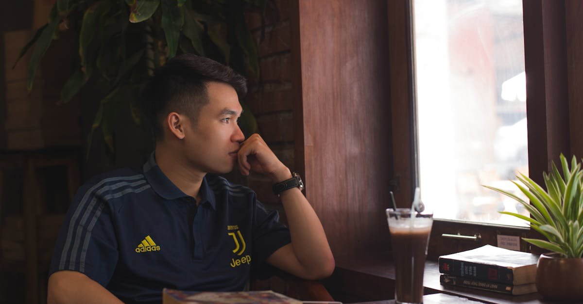 A man thoughtfully gazing outside a cozy restaurant window with a coffee on the table.