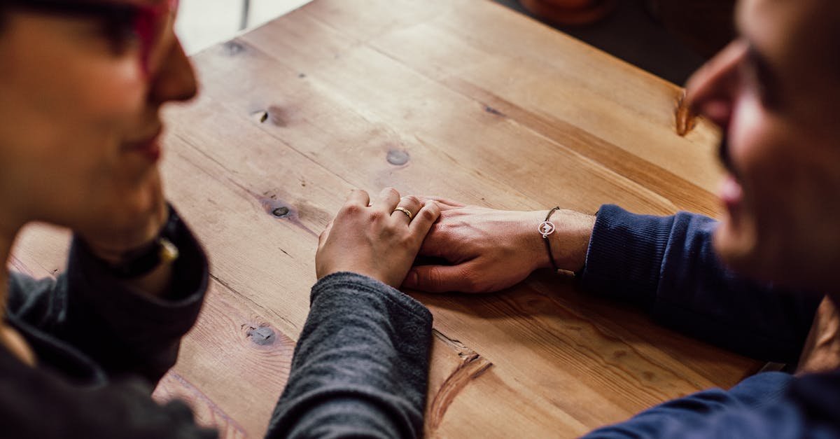 A couple shares a romantic moment holding hands across a wooden table indoors.